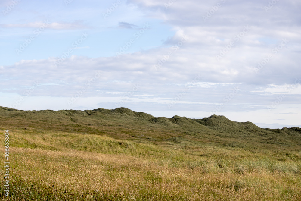 Grassy Hill in front of Blue Sky and Clouds