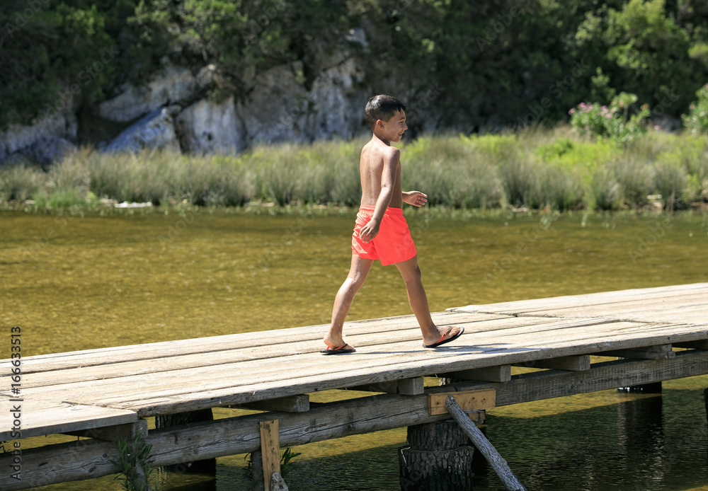 Boy walking on a wooden foot bridge on a lake