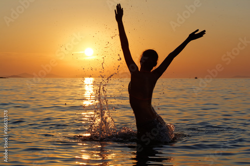 Sylwetka kobiety w wodzie na tle zachodzącego słońca © gpmax