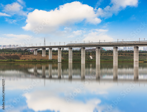 Low Angle View Of High Speed Train On Bridge Over River against cloudy sky.