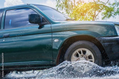 Car runs through flood with water splash during hard rain fall.