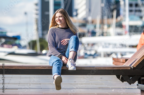 outdoor portrait of young happy smiling teen girl on marine background on a sunny day, auckland central wharf, new zealand