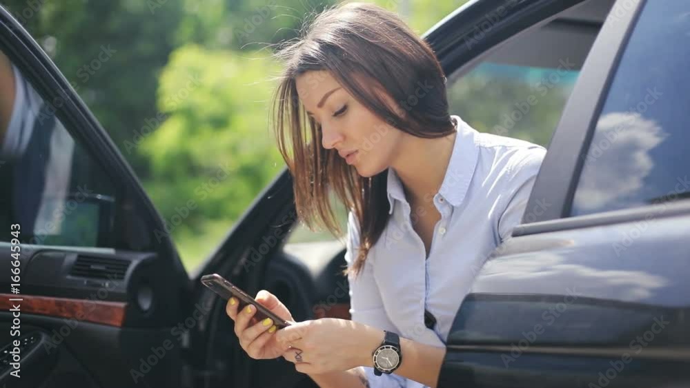 Young woman using holding working mobile smart phone wireless modem lifestyle sitting car open doors communication traffic wristwatch watch attractive checking news online business trip sunny day