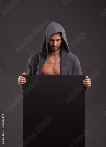 Young pensive man portrait of a confident businessman showing presentation, pointing paper placard black background. Ideal for banners, registration forms, presentation, landings, presenting concept.