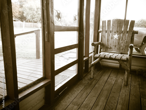 Black   White image of an empty chair on a screened-in porch  with backlighting creating a glowing halo effect  like a memory.