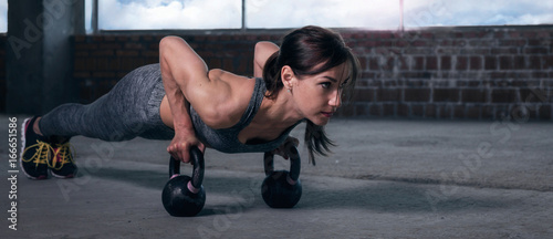 Young woman athlete in sportswear push ups with dumbbells