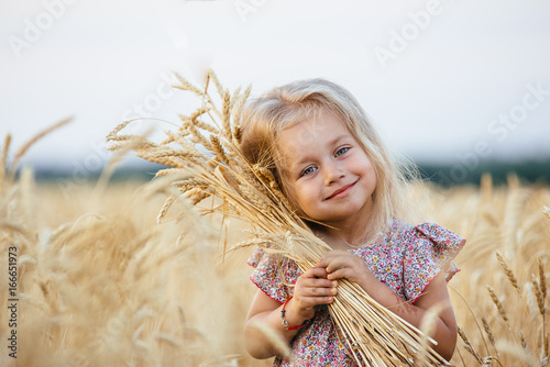 Cute little girl playing in the summer field of wheat