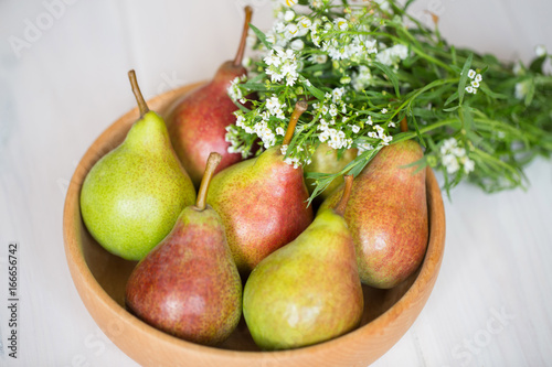 Pears in a wooden plate with white flowers on a light background