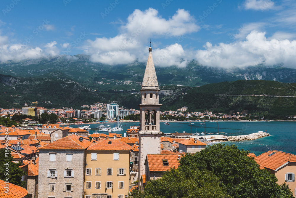  Budva Old town view from above to city roofs, St.John church spire, cloudy mountains and Adriatic sea on background. Tourist capital Budva high view, Montenegro.
