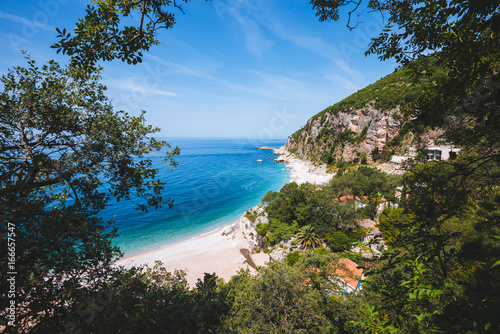 Adriatic sea coast by sunny day summer landscape. Pebble beach  house roofs and green tree brunches under blue sky near Perazica Do village on the way to Petrovac  Montenegro.