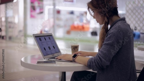 Young woman is looking in the online store for a new smart watch using a notebook