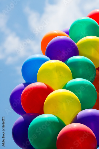 Low angle view of coloured balloons against a blue sky.