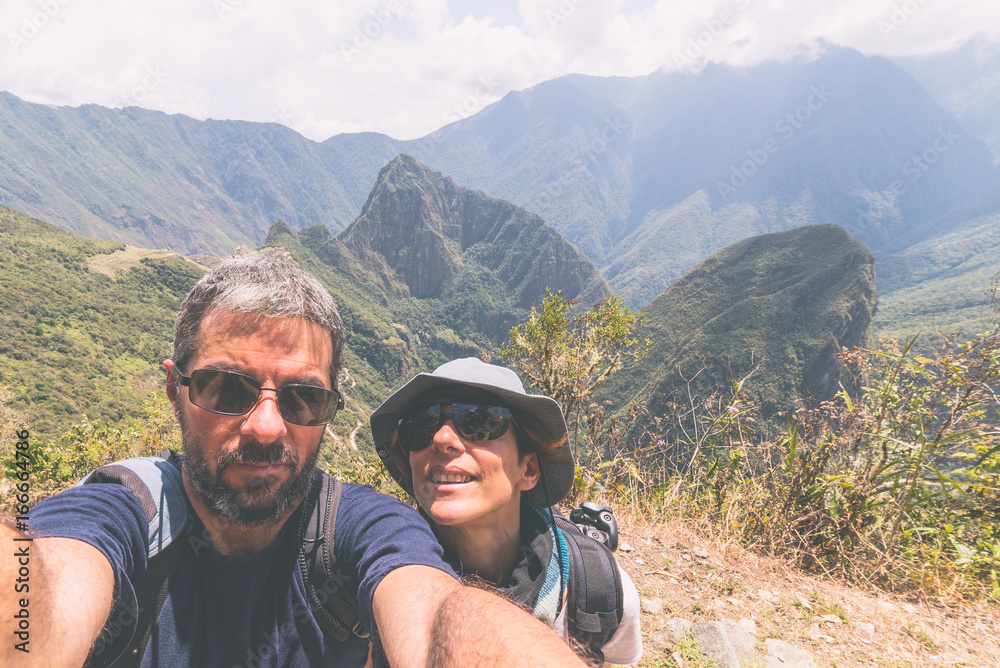 Couple taking selfie on the terraces above Machu Picchu, the most visited travel destination in Peru. Concept of adventures in South America and people traveling around the world. Toned image.