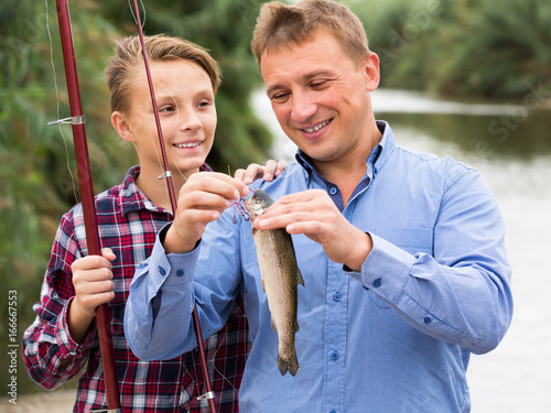 Positive man with son looking at fish on hook photo