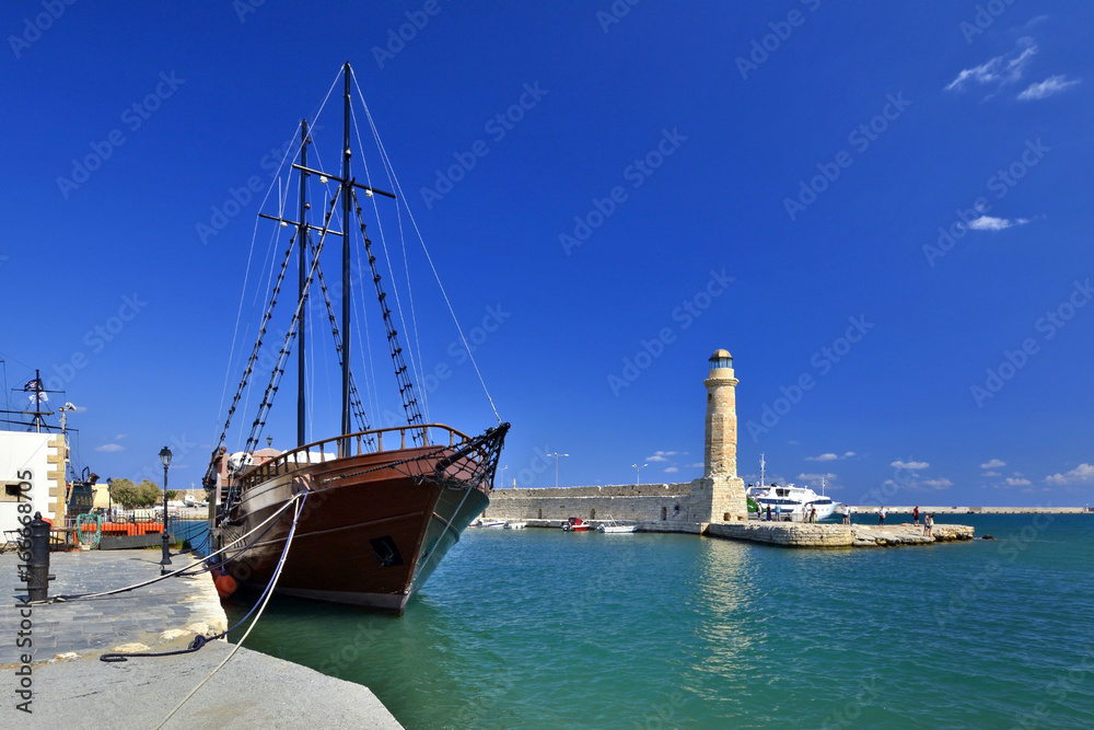 Lighthouse and beautiful old-style wooden ship at the venetian harbor of Rethymno, Crete, Greece Lighthouse and beautiful old-style wooden ship at the venetian harbor of Rethymno, Crete, Greece