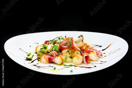 classic Italian summer delicious fresh salad with cheese, parma ham and soy sauce on white plate, on dark background, top view