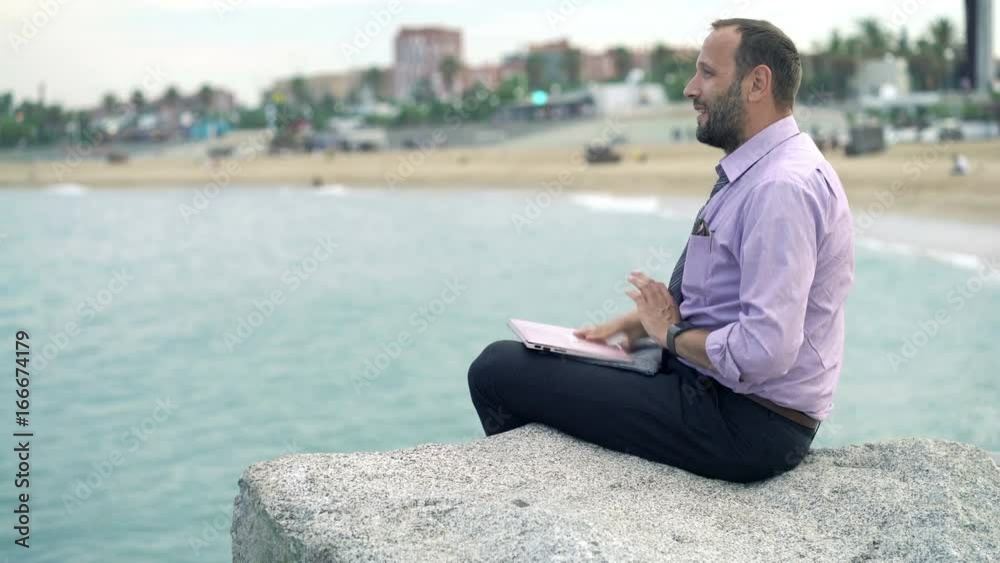 Young businessman finishing work on laptop and relaxing on rock near sea
Young businessman finishing work on laptop and relaxing on rock near sea