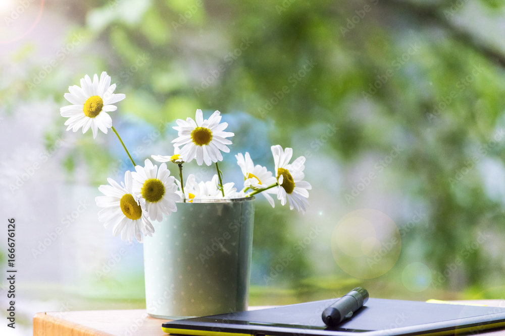 Fototapeta premium Mug, daisies, graphics tablet. The concept of am designer. A Sunny summer morning.