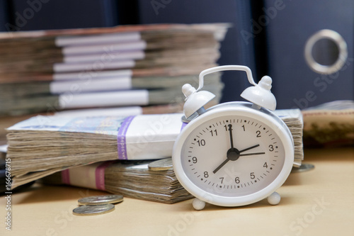 Time is money. An alarm clock and a lot of Russian money on the background of business folder