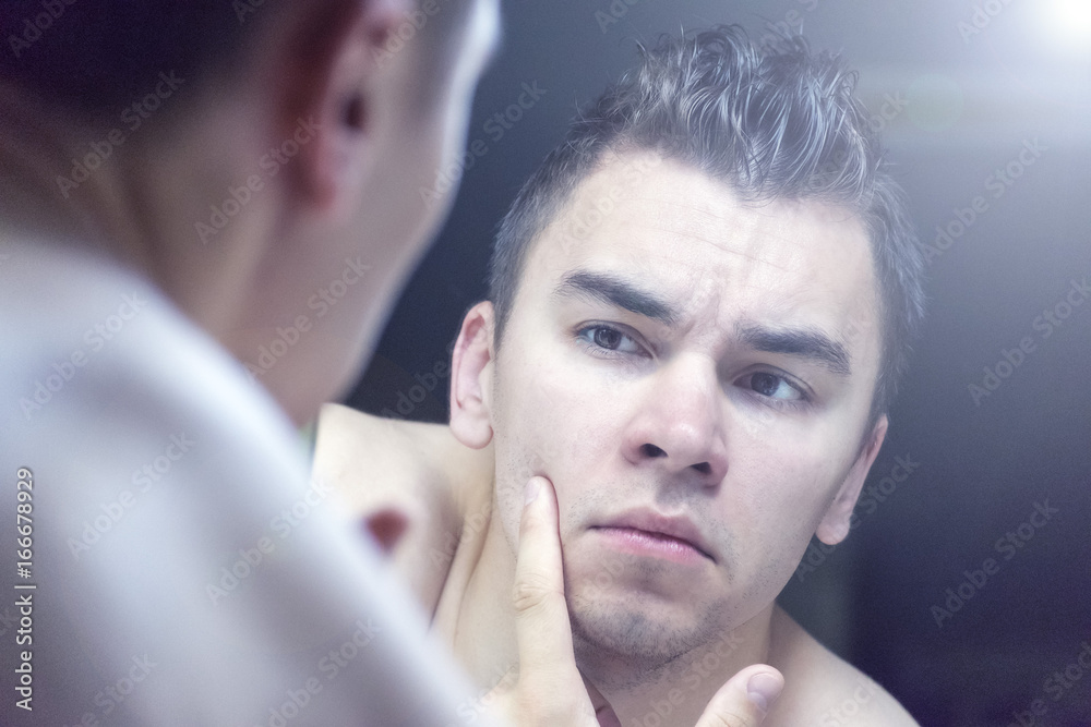 Fototapeta premium The young man looks at himself in the mirror