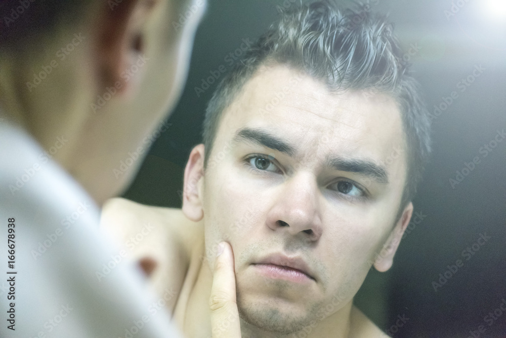 Fototapeta premium The young man looks at himself in the mirror
