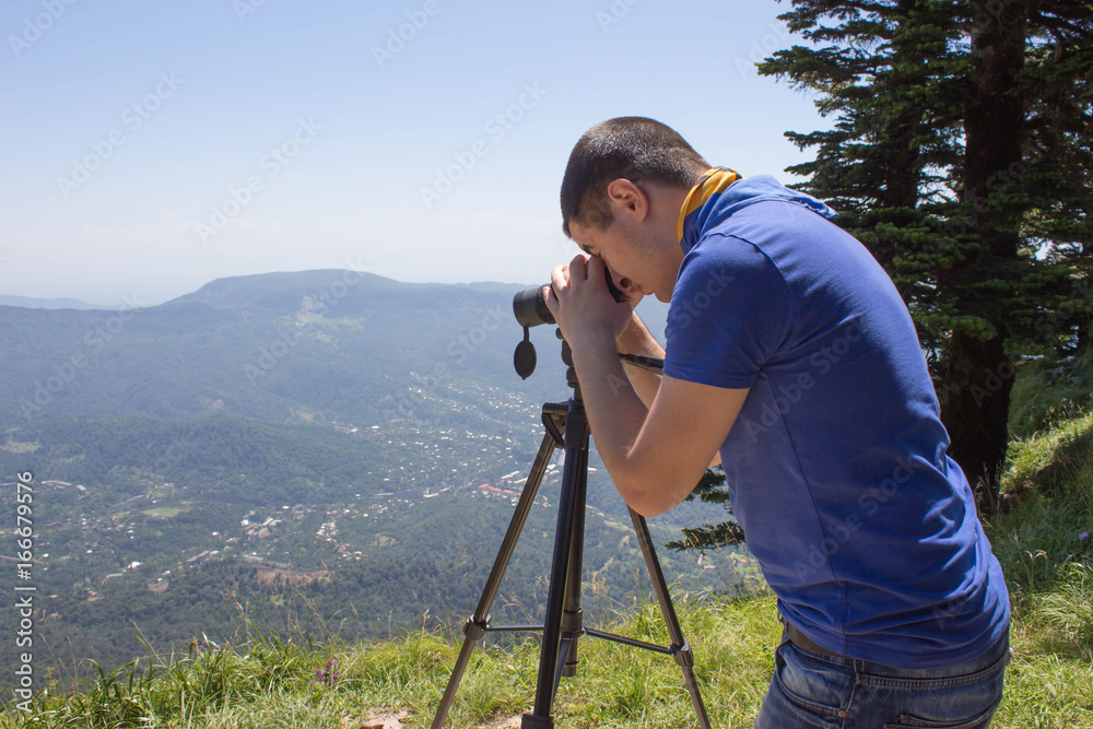 Traveller looking the landscape from the cliff with binoculars tripod