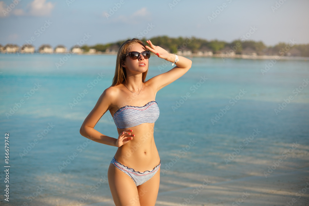 Spa wellness beach beauty woman in bikini swimwear relaxing and sun bathing near blue lagoon. Beautiful peaceful young female model on holiday travel tropical resort. Sun tan cream protection concept