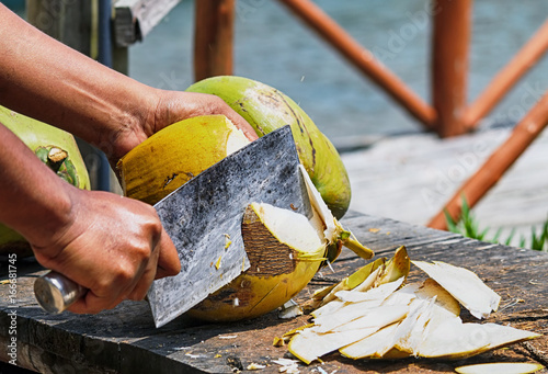 Hands cutting up fresh coconut by large knife.