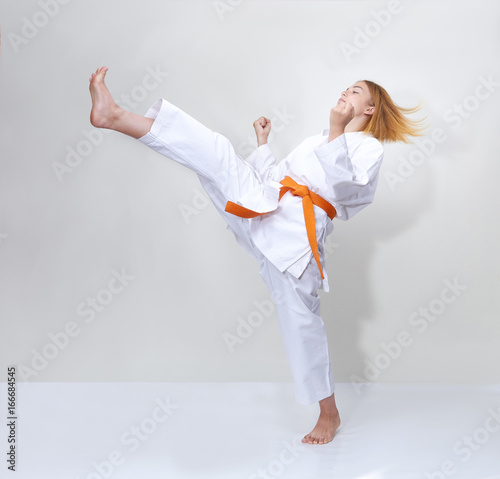 Sportswoman with an orange belt beats a kick on a gray background