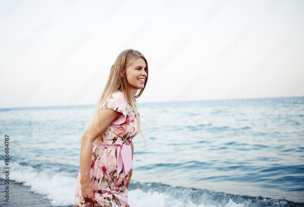 Pretty smiling female in floral dress running on seashore at sunset. Pretty smiling female in floral dress running on seashore at sunset.