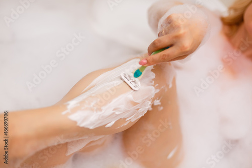 Young and beautiful woman shaving her legs in the bath with foam