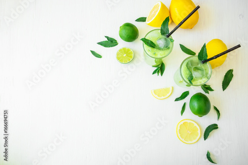 Refreshing drink with cucumber, limes and orange on white wooden table