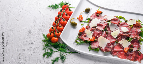 Carpaccio with meat and vegetables. Italian cuisine. On a wooden background. Top view. Free space for your text.