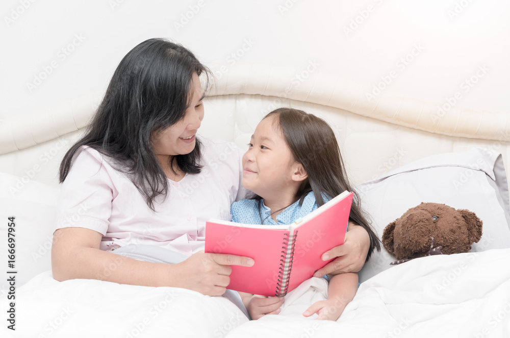 Daughter looking mother reading book on bed Daughter looking mother reading book on bed