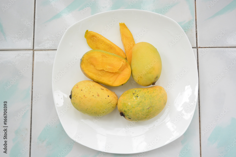 Three whole and 1 cut thai yellow mangoes on a white plate