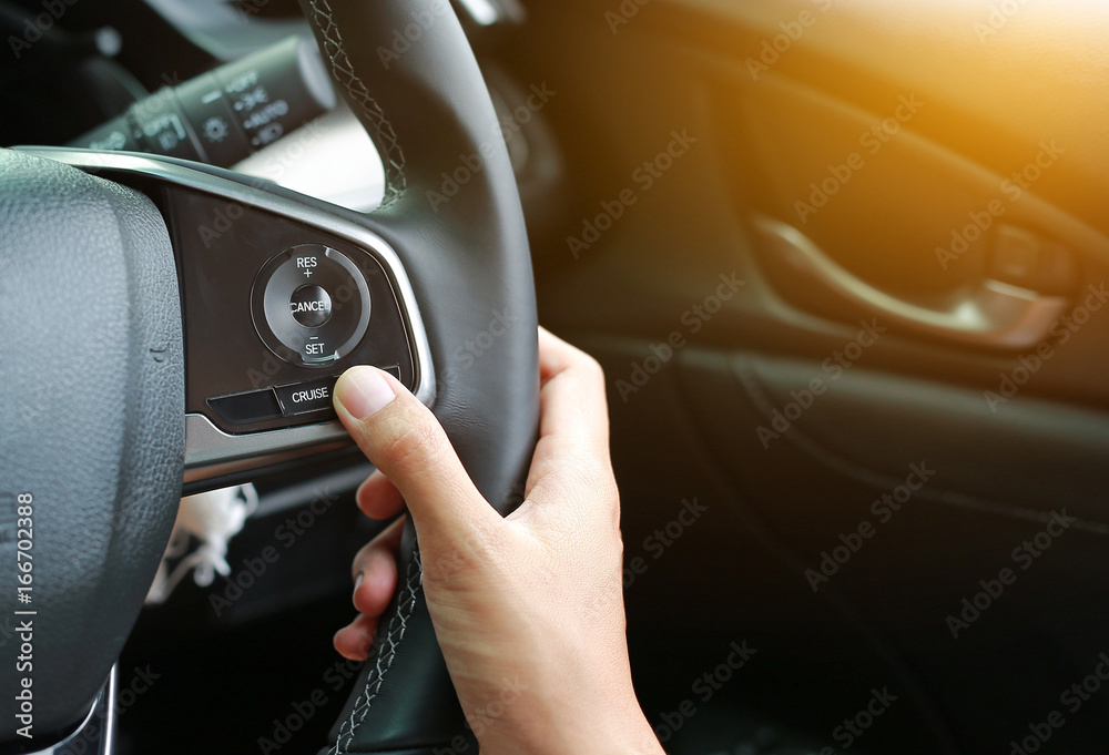 Hand using Cruise control buttons on modern car and speed limitation.