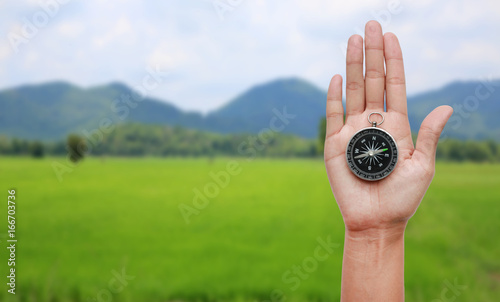 Compass in hand against nature landscape background.