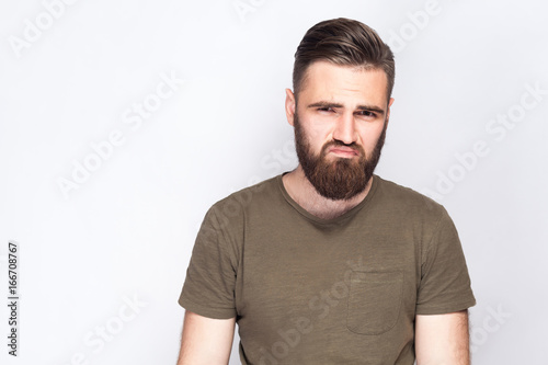 Portrait of unhappy sad bearded man with dark green t shirt against light gray background. studio shot. .