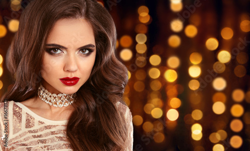 Glamour fashion brunette girl portrait. Long wavy hair style. Red lips beauty Makeup. Sexy model in sequin dress over golden bokeh lights background.