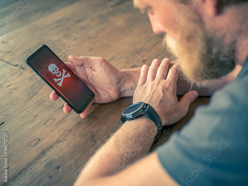 Blond male hold smart phone with virus. Wooden table in backgrund.