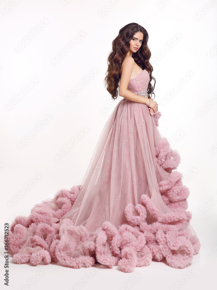 Beautiful woman in luxury lush pink dress. Fashion lady brunette in gorgeous long gown posing isolated on white studio background. Beautiful woman in luxury lush pink dress. Fashion lady brunette in gorgeous long gown posing isolated on white studio background.