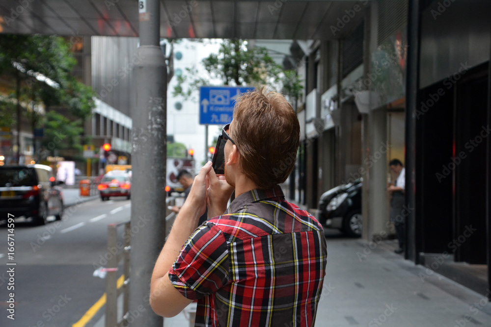 Handsome young man traveling and taking photo with his mobile phone on Hong Kong city.