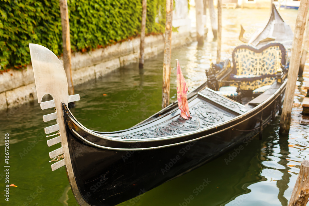 One of famous Venetian gondolas laid up at its moorings against a cityscape with red house and bridge