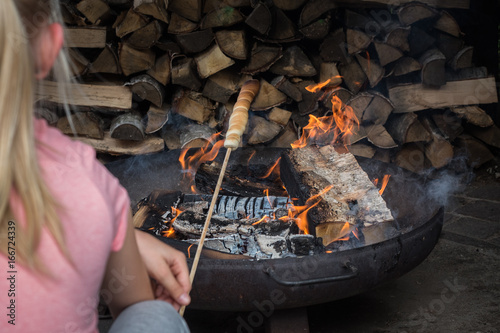 Mädchen von hinten fotografiert am Lagerfeuer mit Stockbrot in der Hand