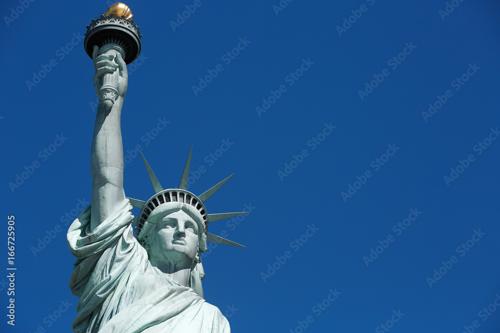 Obraz premium Statue of Liberty with golden torch, blank blue sky space