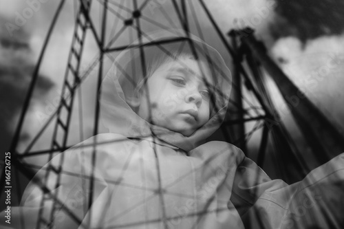 Child gazes sadly through a train window onto which mechanical structures are reflected.