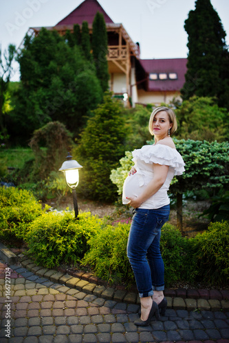 Fabulous pregnant bridesmaid wearing jeans and white t-shirt posing outside at bachelorette party.