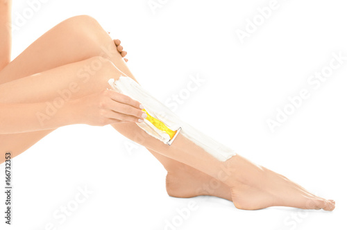 Young woman shaving leg on white background