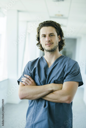 Portrait of confident, happy male nurse in hospital hallway