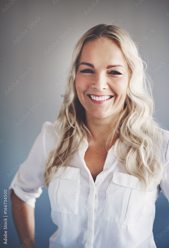 Smiling young blonde businesswoman standing alone in an office Smiling young blonde businesswoman standing alone in an office